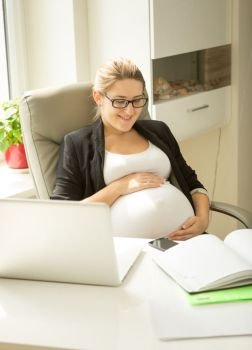 Beautiful smiling pregnant woman posing at office at desk