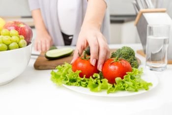 Closeup photo of woman picking fresh tomato from table on kitchen
