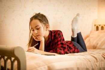 Beautiful smiling teen girl lying on bed and writing in diary