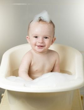 Cheerful laughing 9 months old baby playing in foam at bath