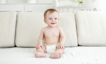 Happy smiling baby boy in diapers sitting on bed at bedroom