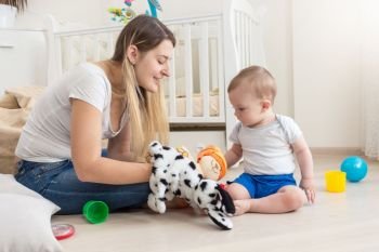Smiling mother wearing dog puppet on hand and playing with her baby boy