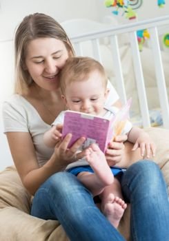 Portrait of baby boy sitting on mothers lap and reading book