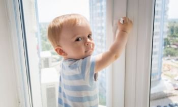 Baby boy pulling by the window handle. Concept of child in danger