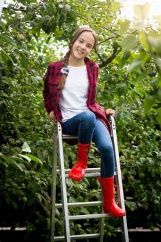 Young girl in red wellington boots  sitting on stepladder at garden