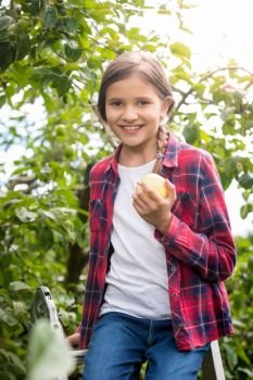 Cute little girl sitting on stepladder at garden and holding fresh apple