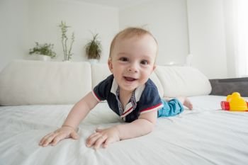 Wide angle image of happy smiling toddler boy lying on bed and looking in camera. Wide angle photo of happy smiling toddler boy lying on bed and looking in camera