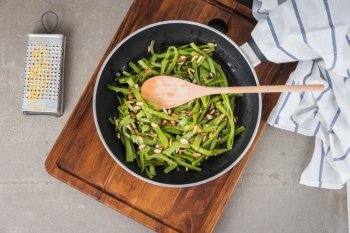 Top view of green beans with roasted almonds on fry pan on kitchen countertop.