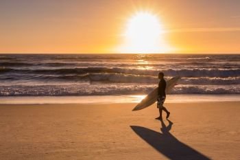 Surfer walking on the beach at sunset in Portugal.