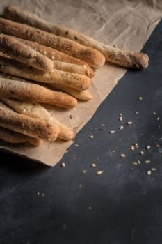 Bread sticks with salt and herbs on dark board.
