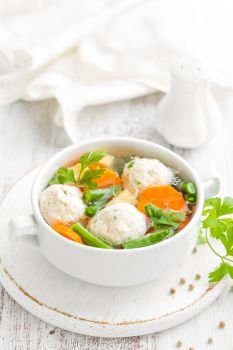 Fresh chicken soup with vegetables and meatballs in a bowl on white background. Top view