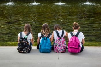 Girls with colorful Backpack Seated in front of Fountain: Rear View