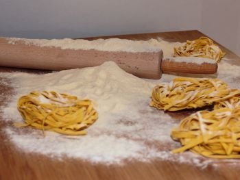 Uncooked Tagliatelle Italian Pasta on Wooden Table with Rolling Pin and Flour