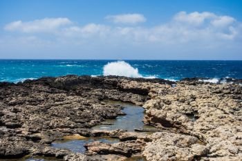 Rocky coastline and tide pools with splashing waves under partly cloudy sky in Malta.