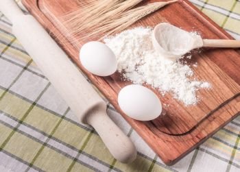 Cutting board with eggs and a hill of flour and a wooden rolling pin lying on a table