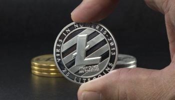 hand showing litecoin with black background with a single litecoin facing the camera in sharp focus with shading on the icon letter B on the face of the bit coin