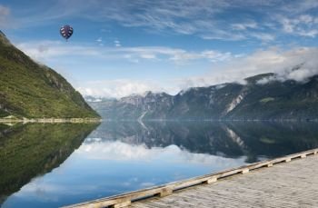 hot air balloon flying over the mountains and in fjord in norway with wooden walking track in front