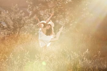 The ballerina doingis arabesk at the meadow In the white dress. At the nature background with the rays of sunset.