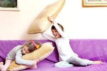 Two girls (sisters) laughing make boxing on pillows
