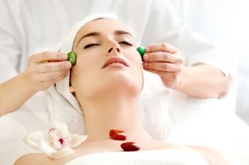 Spa salon: Young Beautiful Woman Having Chakra Facial Massage with Stones .
