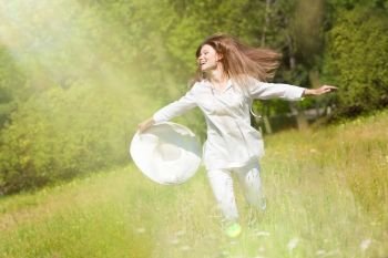 Happy Young Woman Running with a White Hat at the Green Meadow in the White Clothes.
