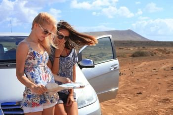 Two young women with car look at road map with mountain landscape in background