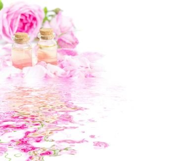 Two vials of rose essential oil, pink roses and rose petals isolated on a white background reflected in the water surface with small waves, with copy-space