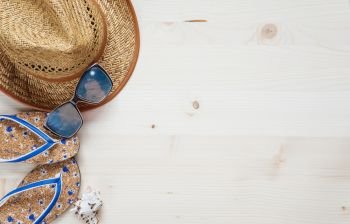 Concept of a beach holiday: slippers, sunglasses, straw hat and seashell are on a light wooden surface. Top view, flat lay