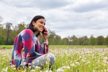 Colombian woman sitting in flowering meadow phoning with mobile phone