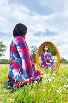 Young colombian woman sits with mirror in flowering pasture