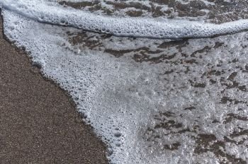 Wave with foam on a sandy beach