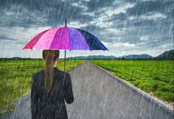 business woman holding multicolored umbrella with falling rain at country road