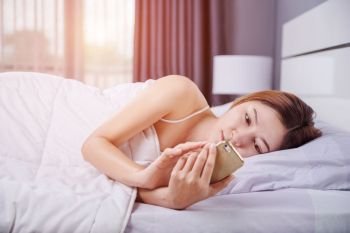 woman using her smartphone on bed in the bedroom with soft light