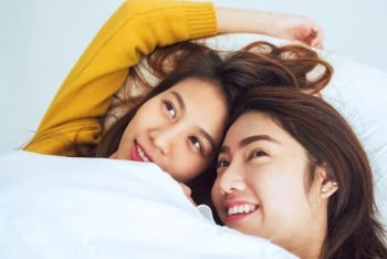 Beautiful young asian women LGBT lesbian happy couple showing surprise and looking at camera while lying in bed under blanket. Funny women after wake up. LGBT Lesbian couple together indoors concept