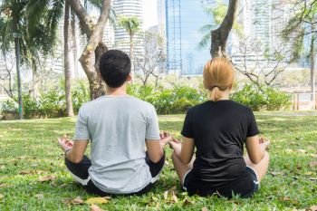 Young love couple making a meditation to calm their mind after exercising in park encircle with a warm light sunshine in afternoon. Yoga Sport and Healthy lifestyle concept. Couple outdoor mind peace.