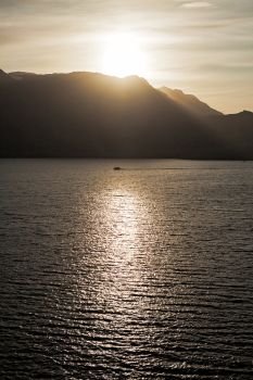 Small boat sailing in the sea at sunset with mountains on background. Small boat sailing in the sea
