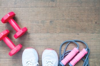 Red dumbbells, jump rope and sport shoes on wood background with copy space, Healthy lifestyle concept