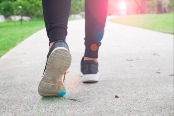 fitness woman walking in public park, closeup on shoe with sunlight