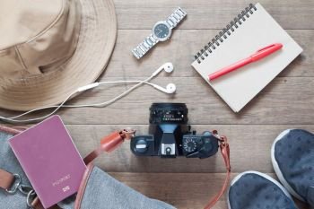 Flat lay of travel items and accessories with camera, earphones on wood background
