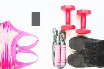 Flat lay of cellphone with pink sport bra, Jump rope and red dumbbells on white background, Workout and Healthy concept, Top view
