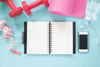 Blank notebook and smartphone with dumbbells, yoga mat, water and measuring-tape on pastel color background, Healthy lifestyle concept 