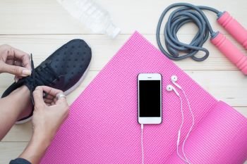 Top view of Healthy Lifestyle concept, woman tying shoes with smart phone on yoga mat