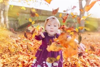 Representative fall image of a child enjoying autumn colors by playing with fallen leaves and throwing them at the camera