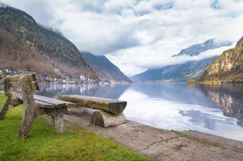 Travel destinations theme image with the Dachstein Mountains reflected in the water of the  Hallstatter lake and wooden benches on its shore, in Hallstatt, Austria.