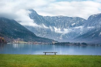 Beautiful scenery with the majestic Northern Limestone Alps, the Hallstatter lake and a wooden bench on its shore, in the famous Hallstatt town, in Austria.