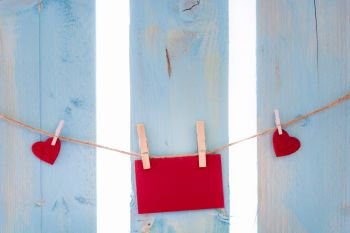 Empty red message card surrounded by red hearts, tied to a linen string with wooden clips, on a blue fence.
