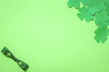 Saint Patrick frame design, with a bunch of paper clovers in a corner and a bow tie in the other, displayed on a blank green paper background.