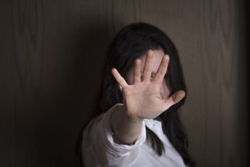 Brunette woman holding her hand stretched out toward the camera, covering her face, avoiding to be seen or stopping a problem.