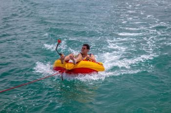 Man sitting in inflatable ring towed by a boat in the water and recording himself with Go Pro camera