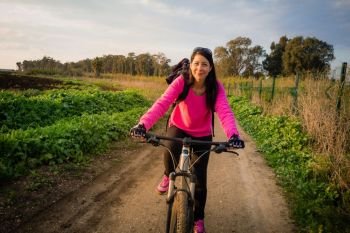Woman riding a bicycle in the countryside and looking at camera.